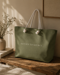 Green tote bag with 'RETURN TO SOURCE' text on a wooden surface with a neutral background