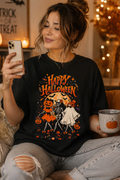 A woman wearing a black graphic t-shirt with a 'Happy Halloween' skeleton illustration, sitting in a cozy room and taking a mirror selfie.