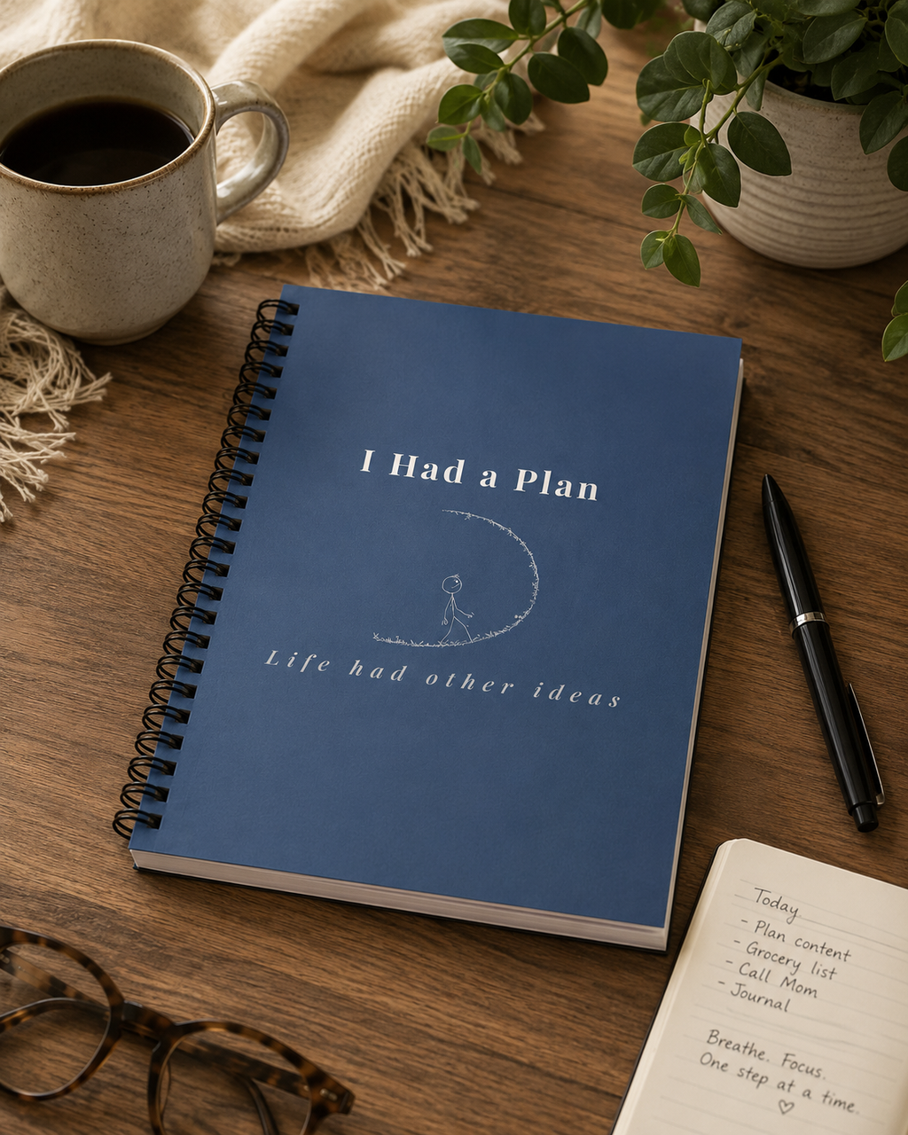 Blue notebook with 'I Had a Plan' text on a wooden table with a cup of coffee and pen.