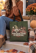 An olive green canvas tote bag with a gnome and autumn-themed graphic, featuring the text 'SOMETHING GOOD IS BREWING.' in white.