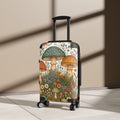 A hard-shell rolling suitcase with an illustrated mushroom and wildflower print, standing upright on a light floor against a beige wall with diagonal shadows.